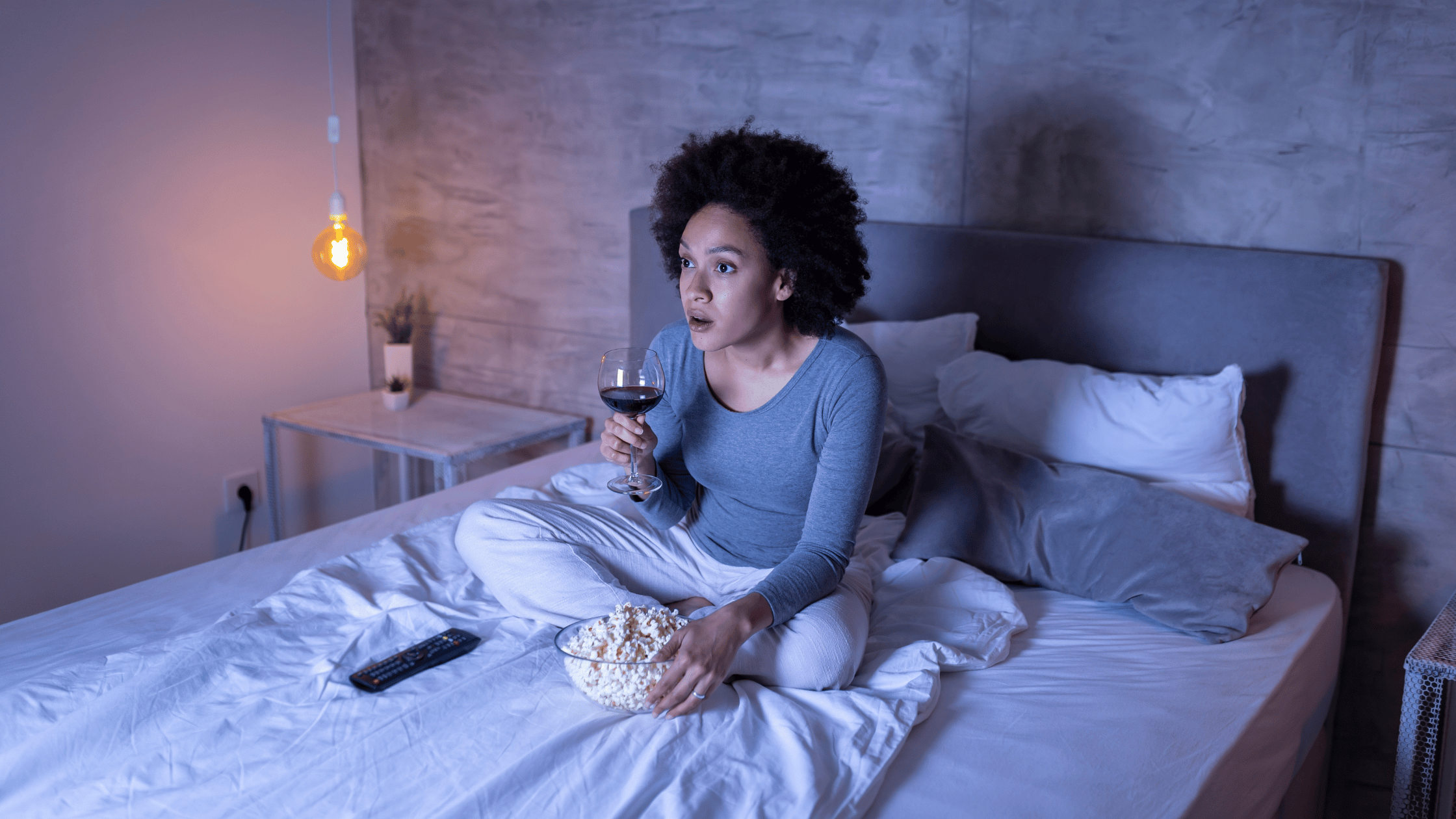 woman-sitting-on-bed-drinking-wine-eating-popcorn-and-watching-tv